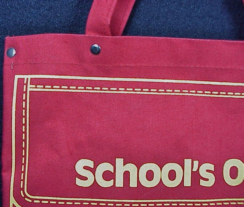 Puede incluir: Bolsa de lona roja con un borde cosido blanco y el texto "School's Out" en blanco.