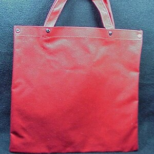 Puede incluir: Una bolsa de lona roja con asa blanca y remaches de metal plateado.