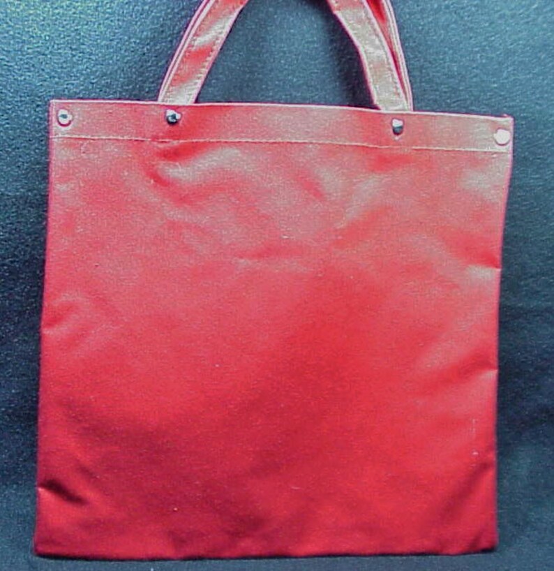 Puede incluir: Una bolsa de lona roja con asa blanca y remaches de metal plateado.