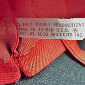 Puede incluir: Una etiqueta blanca con texto negro que dice "WALT DISNEY PRODUCTIONS MADE IN TAIWAN R.O.C. A DIST. BY ALCO PRODUCTS INC."