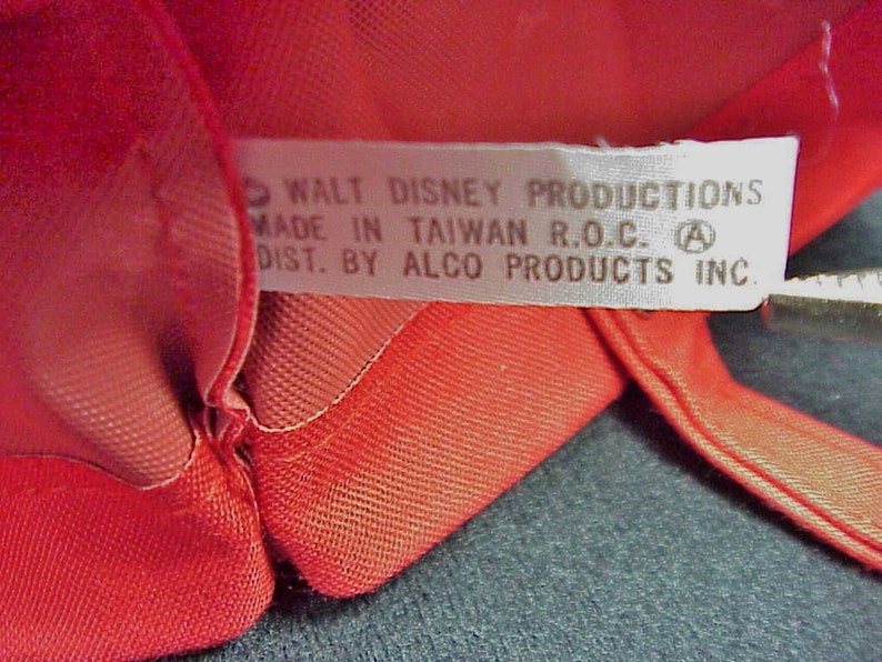 Puede incluir: Una etiqueta blanca con texto negro que dice "WALT DISNEY PRODUCTIONS MADE IN TAIWAN R.O.C. A DIST. BY ALCO PRODUCTS INC."