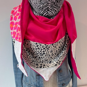 Peut inclure: Une écharpe vibrante avec un mélange de motifs et de couleurs. L'écharpe présente un imprimé zébré, un imprimé léopard et une couleur unie rose vif. L'écharpe est drapée sur une veste en jean, mettant en valeur son design et son style.