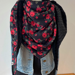 Peut inclure: Une écharpe noire à imprimé floral rouge et doublée de polaire noire. L'écharpe est pliée et drapée sur une veste en jean.
