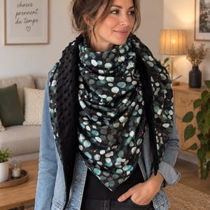 Peut inclure: Un foulard triangulaire présentant un fond noir avec un motif répétitif de feuilles d'eucalyptus bleu sarcelle et blanches. L'envers du foulard est en tissu noir uni avec un motif texturé à pois en relief sur toute la surface.