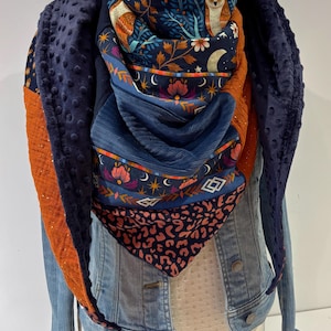 Peut inclure: Écharpe colorée avec divers motifs et textures. L'écharpe présente un tissu bleu foncé texturé sur les bords, avec un centre à motifs représentant des hiboux, des motifs floraux et un imprimé léopard. L'écharpe est drapée sur une veste en jean.