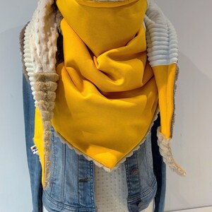 May include: A bright yellow scarf with a soft, textured lining and trim. The scarf is draped over a denim jacket, highlighting its vibrant colour and cosy design. The scarf's texture and colour contrast with the denim.