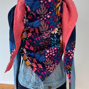 Peut inclure: Une écharpe bleu marine avec un imprimé floral dans des tons de rose, orange et vert. L'écharpe est réversible et a un côté rose avec des paillettes.