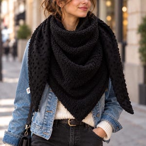 Peut inclure: Un grand foulard triangulaire noir présentant une surface texturée à petits reliefs d'un côté et une matière douce et pelucheuse de l'autre. Le foulard est drapé autour du cou, mettant en valeur sa construction épaisse et chaude.