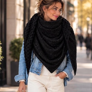 Peut inclure: Un grand foulard triangulaire noir avec un motif texturé à pois et de subtils éclats métalliques. Le foulard est porté sur une veste en jean bleu clair, un pull blanc côtelé et un pantalon crème, formant un ensemble superposé et décontracté.