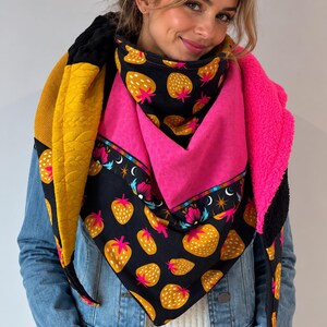 Peut inclure: Un foulard triangulaire composé d'un tissu noir à motifs de fraises jaunes, d'une section rose vif unie, d'un panneau texturé jaune moutarde et d'une doublure en polaire rose éclatant. Il présente une bordure décorative à motifs floraux et étoilés.