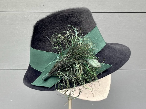 Black long-pile melusine and velour felt brimmed hat with wide green ribbon band and peacock feather ornament