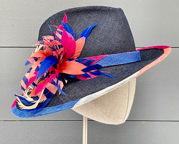 Navy parasisal straw fedora with asymmetrical brim, striped band and binding, and tiger-striped feather spray