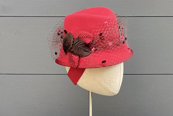 Watermelon red velour felt mini perching fedora with chenille-dotted brown silk veiling and brown and red ribbon cockades and "leaves"