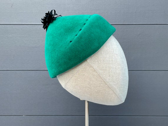 Teal green conical cap with black cross-stitching and cut ribbon ornament