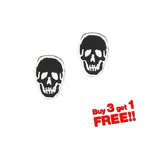 Puede incluir: Dos parches de calavera de hierro negro y blanco. Las calaveras están delineadas en blanco y tienen ojos, nariz y dientes blancos. El texto "Buy 3 get 1 FREE!!" está en letras rojas.