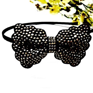 May include: A black headband with a large, sparkly, silver bow. The bow is made of small, round beads.