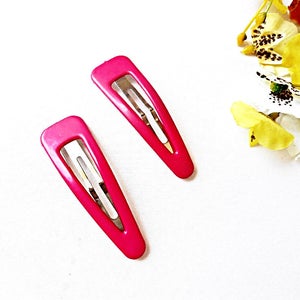 May include: Two pink plastic hair clips with silver metal clasps. The clips are on a white background.