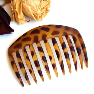 May include: A brown and black leopard print hair comb with a curved shape and nine teeth.