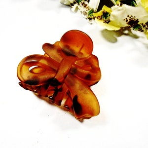 May include: A brown tortoiseshell hair clip with a large bow. The clip is made of plastic and has a shiny finish.