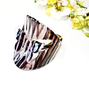 May include: A brown and white striped hair clip with a butterfly design. The butterfly is made of clear plastic with a brown and white striped pattern.