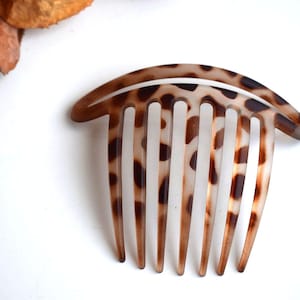 May include: A brown and white leopard print hair comb with five teeth. The comb is curved and has a rounded top.