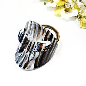 May include: A silver and black butterfly hair tie with a striped pattern. The hair tie is made of metal and has a rubber band.