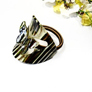 May include: A brown and white striped hair tie with a butterfly design. The butterfly is cut out of the hair tie and has a brown and green color.