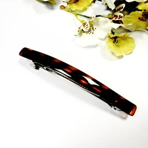 Peut inclure: Une pince à cheveux en écaille de tortue brune avec un fermoir en métal argenté.