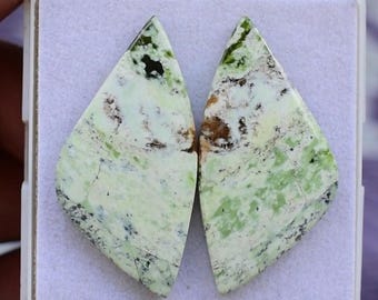 Puede incluir: Dos cabujones de piedras preciosas a juego con forma de diamante. Las piedras tienen un color base blanco cremoso con vetas verdes y marrones. Se presentan en una caja de plástico blanca con interior morado.