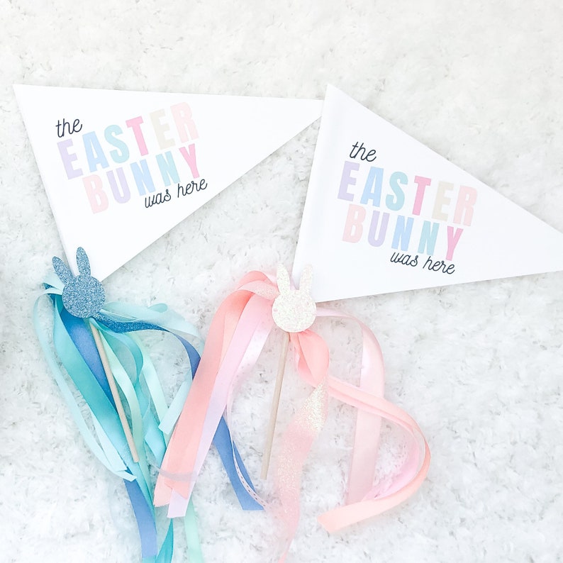 Pu&ograve; includere: Due bandierine a pennant color pastello con il testo "the easter bunny was here" in lettere arcobaleno. Ogni bandierina &egrave; attaccata a un bastoncino con una testa di coniglio scintillante e un lungo nastro.