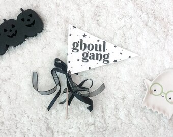 May include: A white triangle flag with black stars and the text "ghoul gang" in black. The flag is attached to a wooden stick and has black ribbon tied around it.