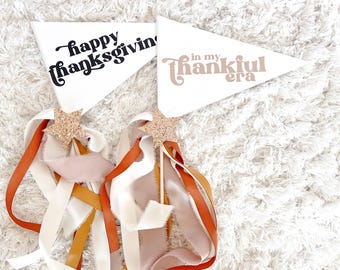 Könnte beinhalten: Zwei weiße Wimpelflaggen mit schwarzem und braunem Text auf einer weißen, flauschigen Oberfläche. Der Text auf den Flaggen lautet "happy thanksgiving" und "in my thankful era".