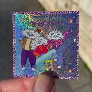 Peut inclure: Autocollant holographique avec une bordure léopard. Il présente trois personnages de dessins animés aux cheveux en forme de nuage, vêtus de tenues colorées. L'autocollant indique "ENOUGH GIRLS TO SAY ALL MEN". Le fond est scintillant avec des étoiles.