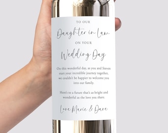 Puede incluir: Una botella de vino blanco con una etiqueta personalizada que dice "A nuestra nuera en su día de boda." La etiqueta también incluye un mensaje deseando lo mejor a la pareja y una firma de Marie y Dave.