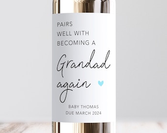 May include: A white wine bottle with a label that reads "Pairs well with becoming a Grandad again" with a blue heart. The label also includes the text "Baby Thomas Due March 2024".