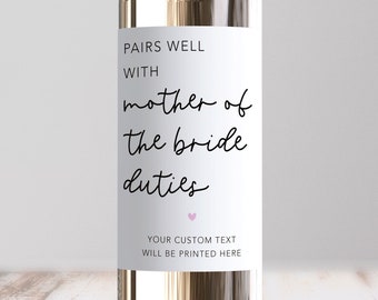 May include: White wine bottle with a label that says "Pairs well with mother of the bride duties". There is a small pink heart at the bottom of the label. The label also says "Your custom text will be printed here".