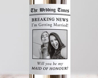 May include: A glass bottle with a white label featuring the text The Wedding Times, BREAKING NEWS I'm Getting Married!, and Will you be my MAID OF HONOUR? The label includes a black and white photograph of two people posing together.