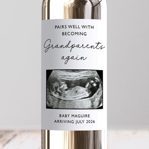 May include: A clear wine bottle with a label that reads "Pairs Well With Becoming Grandparents Again." The label also features a sonogram image and the text "Baby Maguire Arriving July 2026."