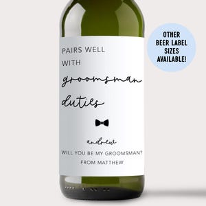 May include: A green glass bottle with a white rectangular label featuring black text that reads PAIRS WELL WITH groomsman duties, a small black bow tie icon, the name andrew, and the text WILL YOU BE MY GROOMSMAN? FROM MATTHEW.