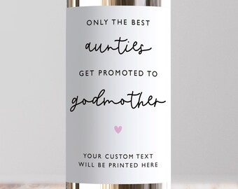 以下が含まれることがあります： ワインボトルの白いラベル。テキストは「ONLY THE BEST aunties GET PROMOTED TO godmother」と書かれています。テキストの下には小さなピンク色のハートがあります。ラベルの下部には「YOUR CUSTOM TEXT WILL BE PRINTED HERE」と書かれています。