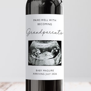 May include: A wine bottle with a custom label announcing a pregnancy. The label reads "PAIRS WELL WITH BECOMING Grandparents" above an ultrasound image. Below the image, it says "BABY MAGUIRE ARRIVING JULY 2026".