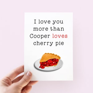 May include: A white card with black text that reads "I love you more than Cooper loves cherry pie". A slice of cherry pie is pictured below the text.