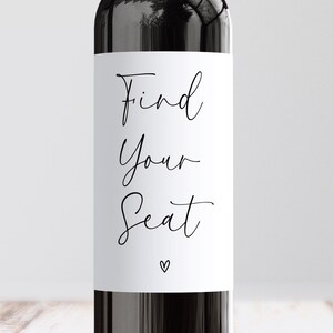May include: A black bottle with a white label. The label features the words "Find Your Seat" in elegant cursive script, with a small heart symbol below. The overall design is simple and modern.