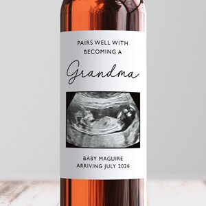 May include: A wine bottle with a white label. The label says "Pairs Well With Becoming a Grandma" and features an ultrasound image. It also reads "Baby Maguire Arriving July 2026."