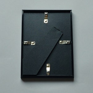 May include: Black picture frame with a black mat and silver hanging hardware.
