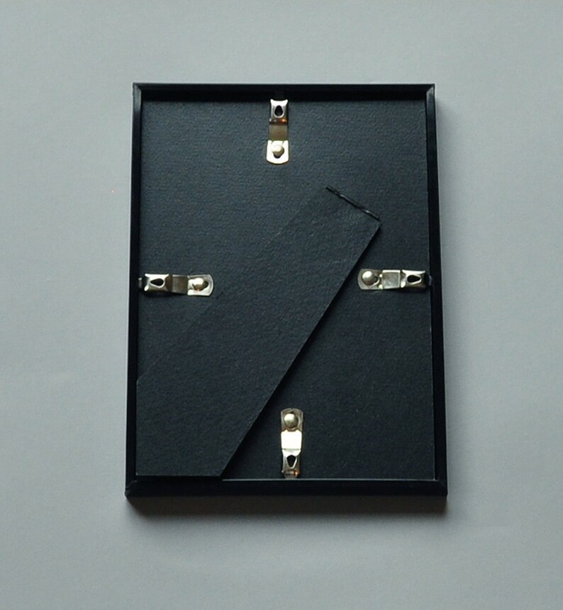 May include: Black picture frame with a black mat and silver hanging hardware.