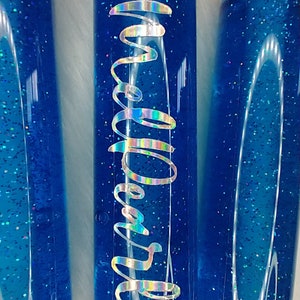 May include: Three blue glass bottles with glitter inside. The middle bottle has the word "Melted" written on it in a silver iridescent font.