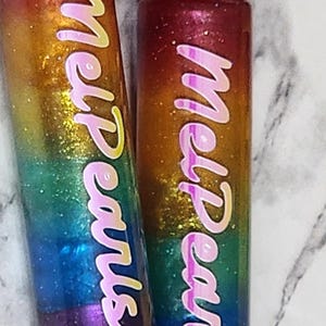 May include: Two clear lip gloss tubes with gold lids and rainbow glitter. The tubes are labeled "Melt Pearls" in pink lettering.