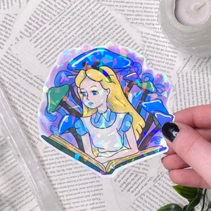 Puede incluir: Una pegatina hologr&aacute;fica con Alicia en el Pa&iacute;s de las Maravillas sentada con un libro en un campo de setas azules y moradas. La pegatina tiene un acabado iridiscente arco&iacute;ris.
