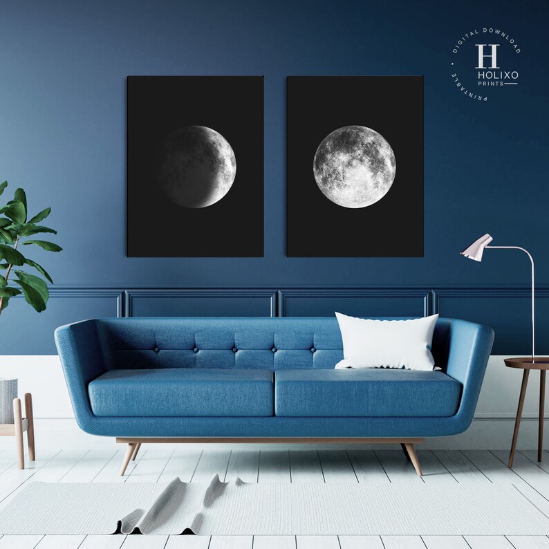 May include: Two black and white prints of the moon in different phases. The prints are framed and hanging on a dark blue wall above a blue sofa.